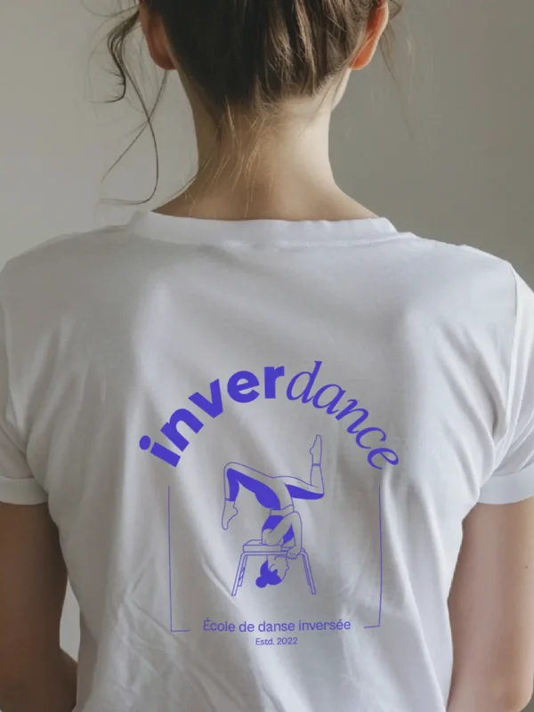 Logo complet de la marque inverdance : en haut la danseuse inversée sur son tabouret, le nom inverdance avec le copyright et la mention école de danse inversée, estd. 2022 en violet sur un t-shirt blanc